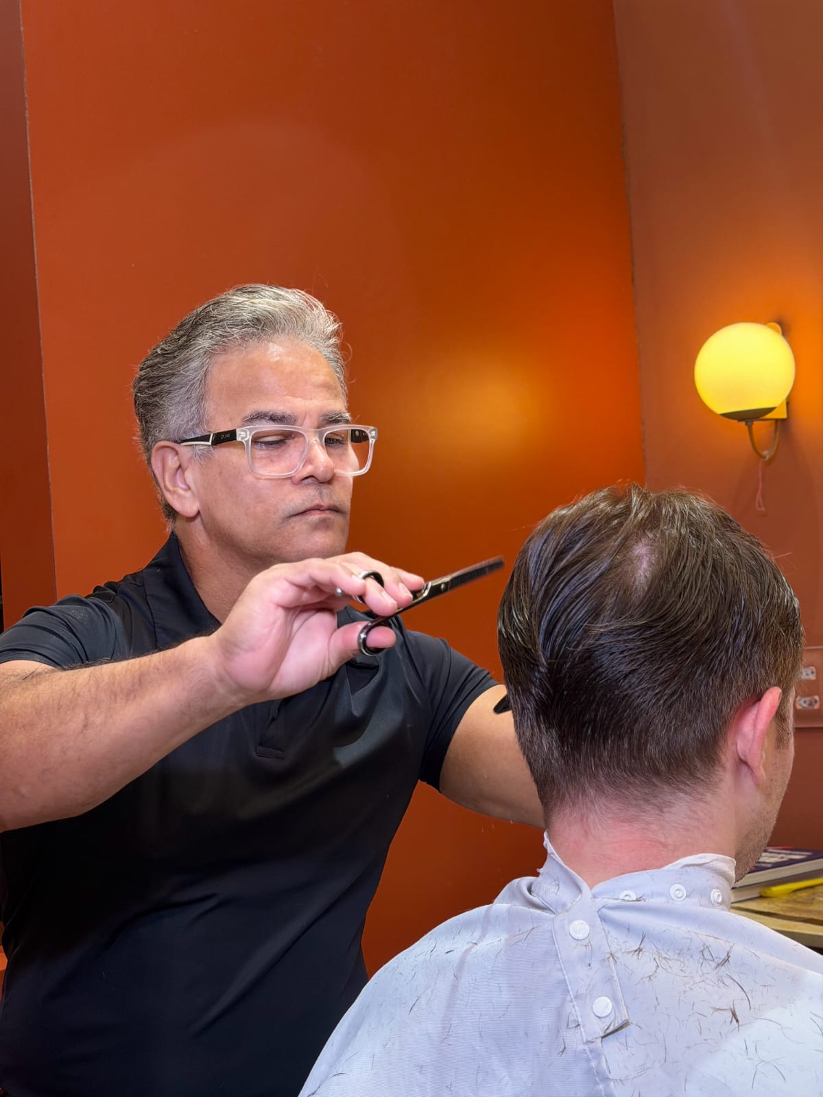 Santos cortando o cabelo de um cliente com tesoura na barbearia.